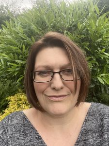 selfie of Michelle Evans, learning disability nurse, against leafy backgroud, Michelle has a brunette bob, glasses and is smiling
