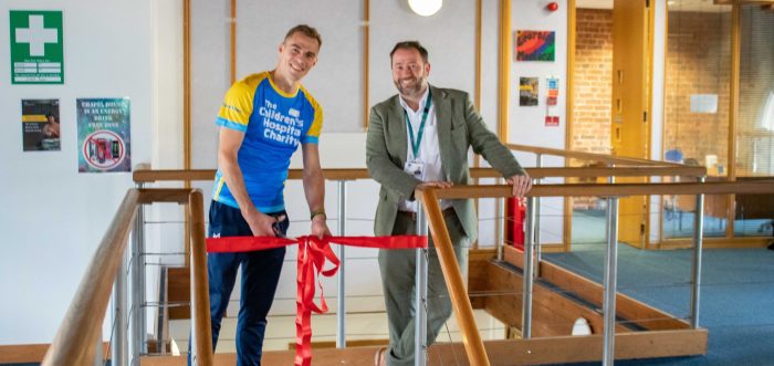 childrens hospital charity patron nick matthews with yellow and blue charity top next to headteacher of becton school cutting red ribbon with scissors