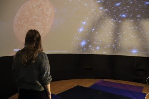 One person standing looking at planets and stars on a screen