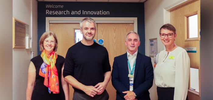 Four people are standing in a hospital corridor in front of a door which says 'Welcome to Research and Innovation'.