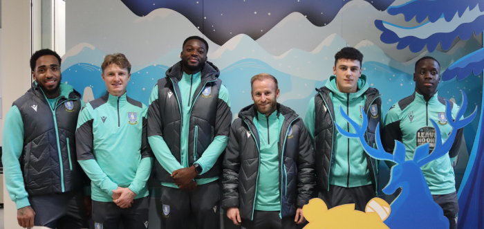 A team of footballers are standing in front of a festive scene in a hospital.