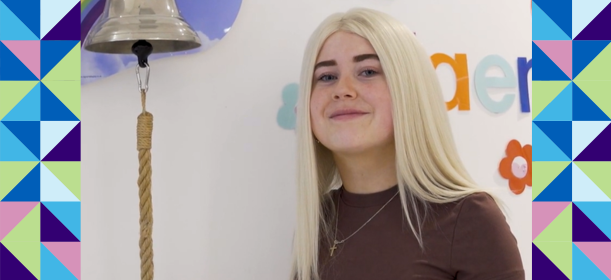Mia smiles whilst standing next to a bell