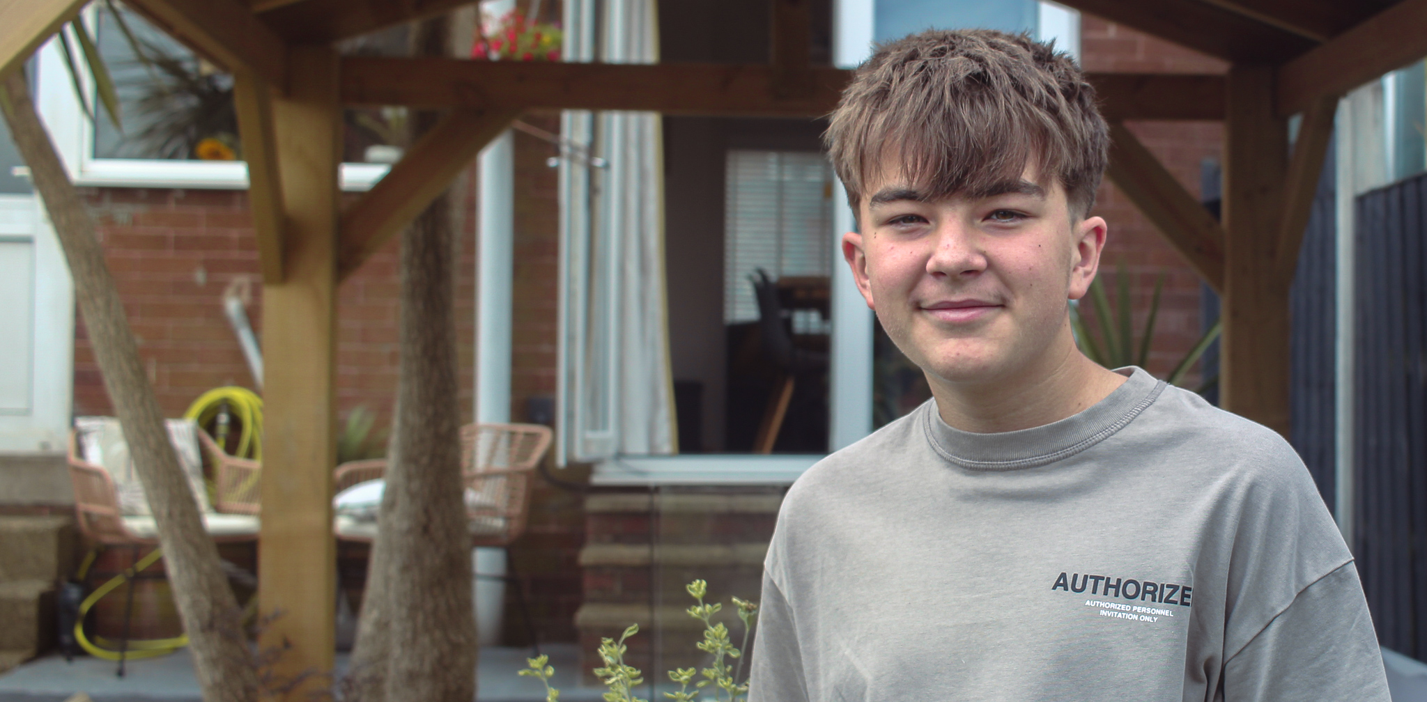 Oscar stands and smiles in front of a wooden structure in his garden